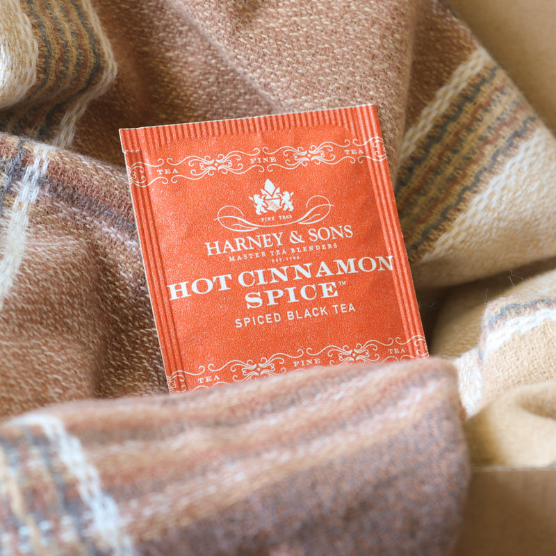 Harney & Sons Hot Cinnamon Spice tea package inside a cardboard box with plaid fabric.