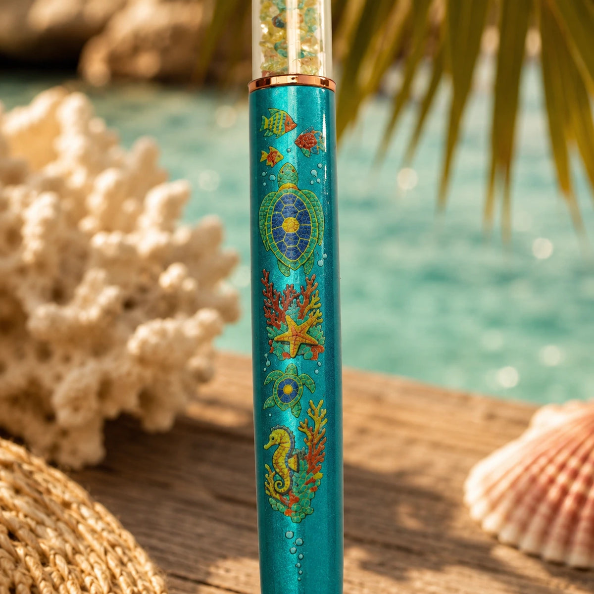 PenGems - Turtle Bay - crystal pen close-up of the full mosaic barrel design, a sea turtle, fish, coral, starfish, second turtle, and seahorse, with blurred turquoise water and a palm frond in the background.